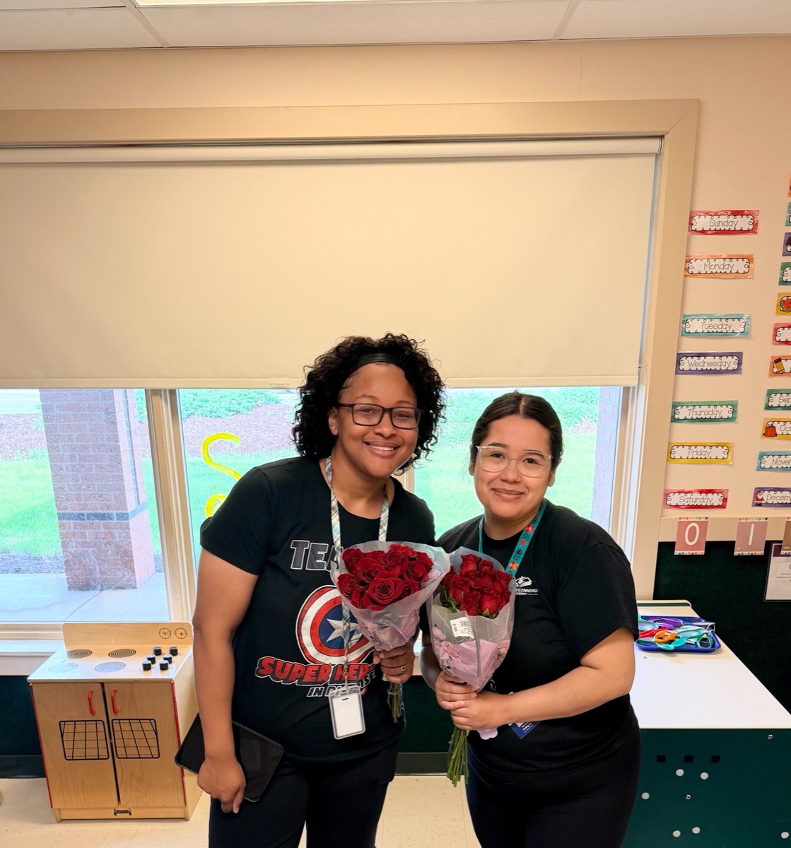 Two teachers holding bouquets of red roses in their classroom